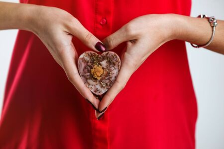 Woman wears red shirt holds decorative aromatic heart shape soap on white backgroundの写真素材