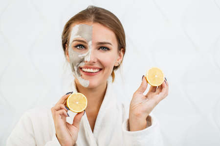 Lovely, smiling girl having fun with two halves of lemon, indoor shot in the white background