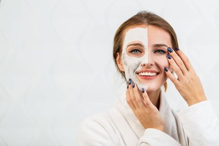 Beautiful girl smiling while applying a clay face mask, isolated shot in the white backgroundの写真素材