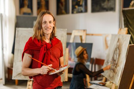 Long hair caucasian male artist smiles near the picture in the studioの写真素材
