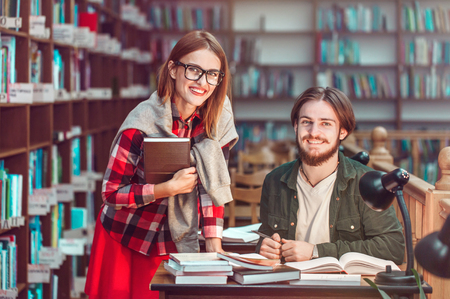 Portrait of two successful students casual stylish, boy and girl in library reading hall, evening time, education conceptの写真素材
