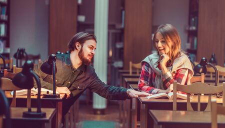 Portrait of two successful students casual stylish, boy and girl in library reading hall, evening time, education conceptの写真素材