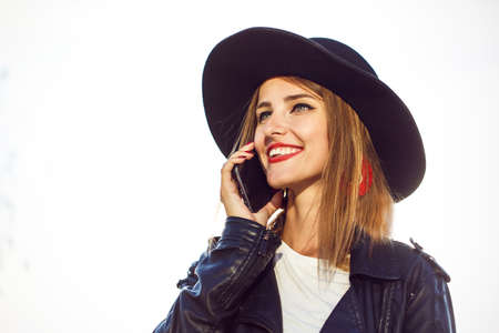 Stylish hipster girl wears black leather jacket and hat talking by phoneの写真素材
