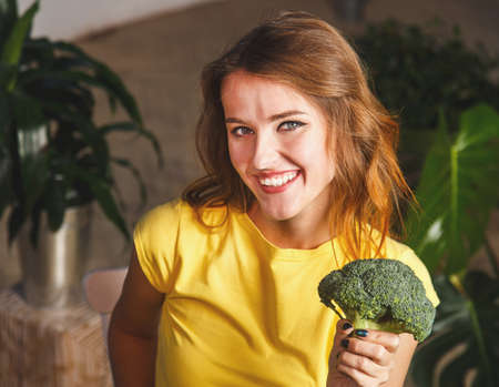 Smiling girl enjoys broccoli, a green pepper and an apple at the table with lots of healthy food, healthy food conceptの写真素材