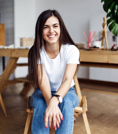 Portrait of young beautiful girl wears white t-shirt sitting on wooden chair indoorの写真素材