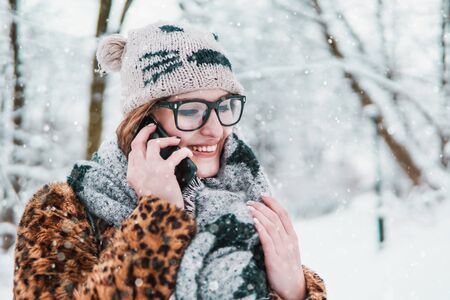 Attractive girl wears glasses talking by smartphone in winter snowy parkの写真素材