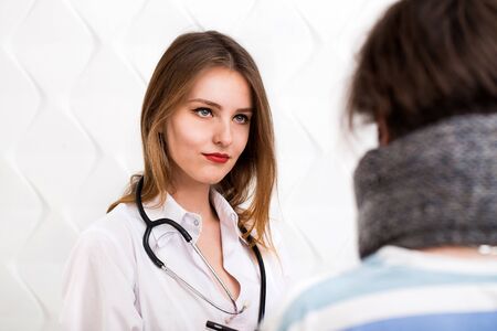 Intelligent young doctor asking questions about illness, patient - handsome boy with a moustache in warm gray scarfの写真素材