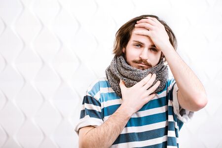 Portrait of a sick man, dark-haired boy with a moustache wearing knitted scarf, indoor shot in white backgroundの写真素材