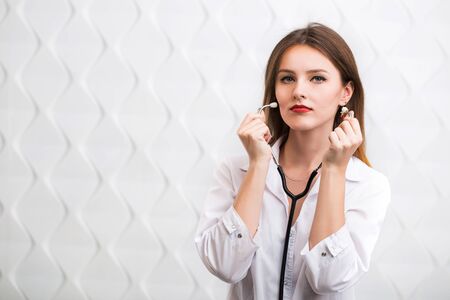 Female doctor holding stethoscope, wearing doctors smock, cheerful caucasian woman isolated before white backgroundの写真素材