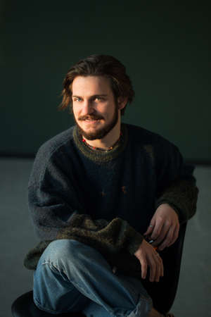 Portrait of hadsome young bearded stylish man sitting on the chair in studioの写真素材