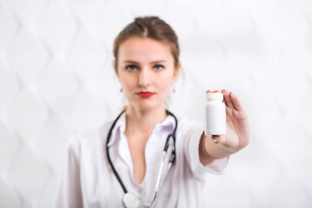 Slim young girl in white doctors smock holds bottle with drugs, indoor isolated shotの写真素材