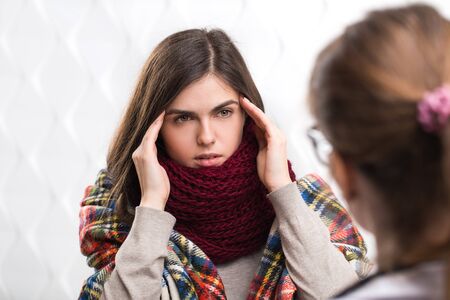 Intelligent doctor asking sick patient about illness, beautiful brunette with headache wrapped in blanket telling about symptomsの写真素材