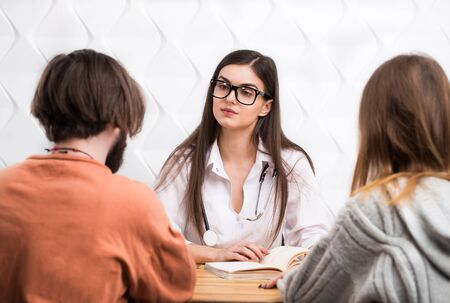 Intelligent caucasian female doctor talking to a couple: bearded, dark-haired man and long-haired womanの写真素材
