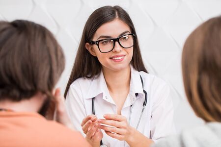 Intelligent caucasian female doctor talking to a couple: bearded, dark-haired man and long-haired womanの写真素材