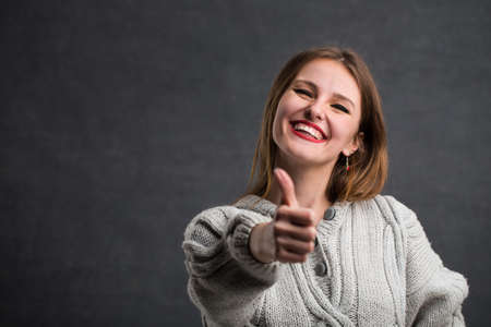Portrait of smiling caucasian girl showing thumb up, long-haired girl posing joyfully in the gray backgroundの写真素材