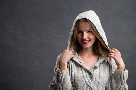 Portrait of beautiful girl in gray sweater playing with her hair, indoor shot in the gray backgroundの写真素材