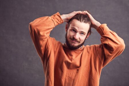 Portrait of serious, handsome man with a dark beard, wearing casual orange shirt, stressed and tired, indoor shot in the gray backgroundの写真素材