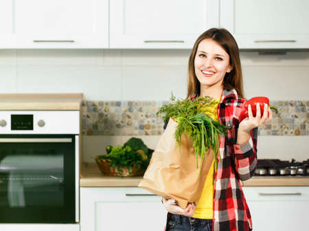 Satisfied caucasian woman, in casual checked shirt, holding shopping pack with fresh, organic food and red pepperの写真素材