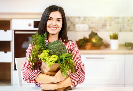 Lovely slim woman, in checked red shirt holding shopping bag with green food, concept of consuming healthy foodの写真素材