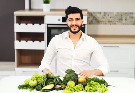 Happy handsome man in white shirt sitting at the table full of green healthy foodの写真素材