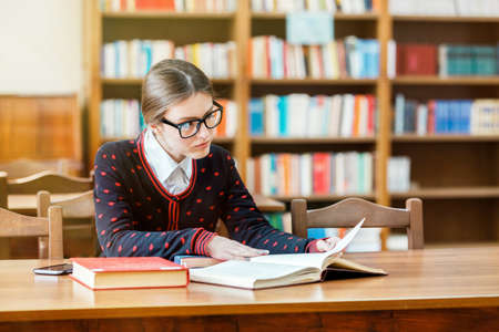 Concentrated student studying in library, young good-looking woman reading books attentively,...