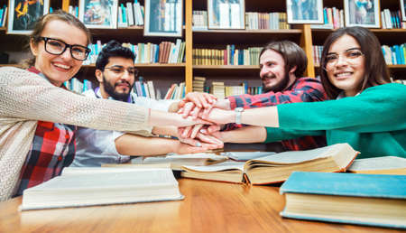 Students working in team, four lovely guys sitting around the brown table full of different books,...