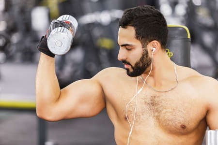 Sexy topless bearded man wears black sport gloves holds metal dumbbell in the gymの写真素材