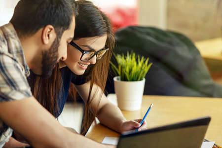 Team collaboration between girl and bearded boy working on table with documents and laptopの写真素材