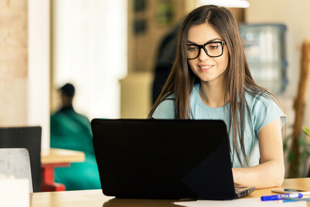 Beautiful dark hair girl student working on the laptop in modern stylish coworking office, successful business conceptの写真素材