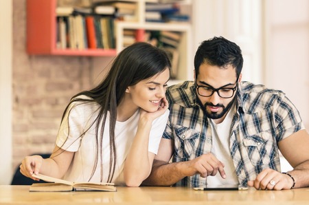 Couple of students study with tablet computer and book sitting in modern stylish room with bookshelves on backgroundの写真素材
