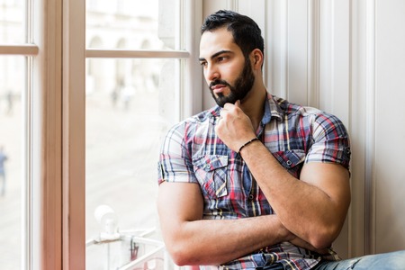 Portrait of handsome bearded man sitting on wide white windowsillの写真素材