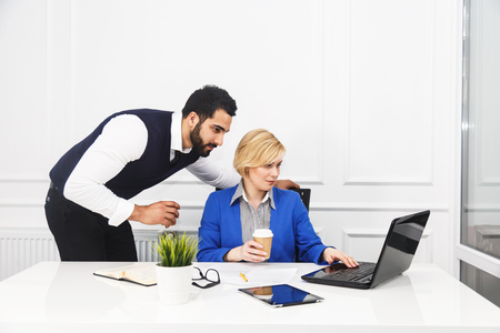 Two business colleagues work with laptop holding cups of coffee in white office interiorの写真素材