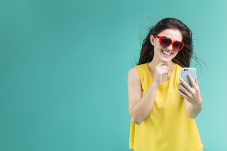 Beautiful smiling brunette girl wears yellow t-shirt and sunglasses making selfie by smartphone...