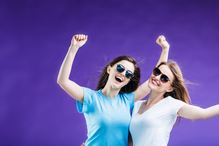 Cute smiling girls dressed in t-shirts and sunglasses before blue backgroundの写真素材