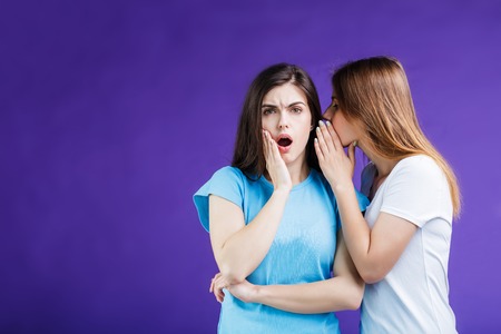 Two pretty women gossipping with face reaction expression before blue background