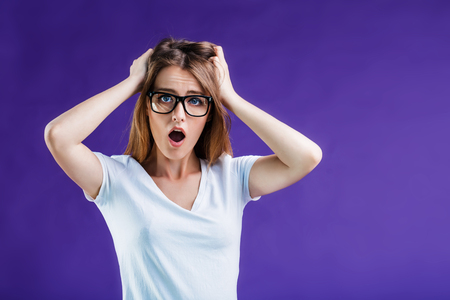Portrait of woman dressed in white t-shirt and eyeglasses make shock grimace on face, isolated on blue studio backgroundの写真素材