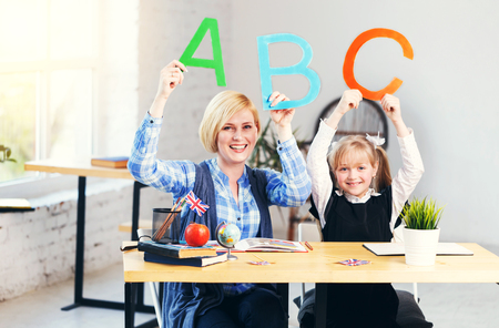 English teacher have fun playing with letters and words with smart school girl, table with books in light classroom with flowerpotsの写真素材
