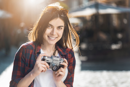 Cute brunette hipster smiling girl holding retro old photo camera, sunset outdoor portraitの写真素材