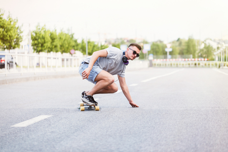 Skateboarder in sunglasses rides longboard on asphalt road in the cityの写真素材