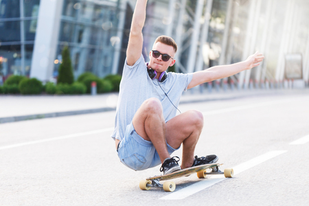Skateboarder in sunglasses rides longboard on asphalt road before modern building in the city, low position trick rideの写真素材
