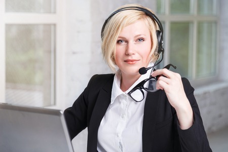 Pretty blonde woman, call center operator dressed in black stylish suit with headset earphones...
