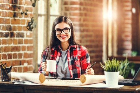 Young pretty long-hair woman engineer drinking coffee after a meeting in the loft modern officeの写真素材