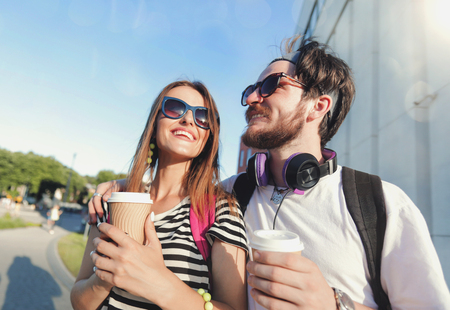 Cute best friends walking at the sunset on the street and drinking coffee, they speaking and listening musicの写真素材