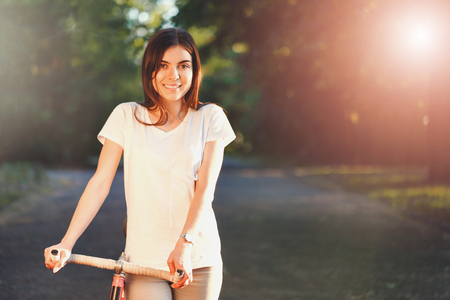 Portrait of pretty romantic girl walking with bicycle on the sunset in green summer parkの写真素材