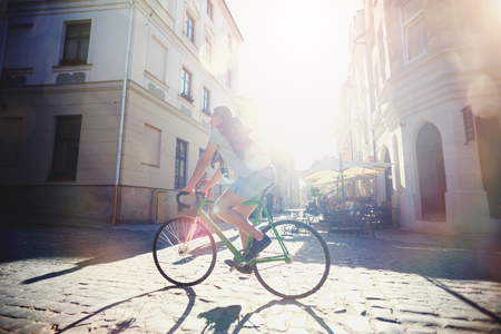 Young hipster light-hair boy in glasses ride green bicycle at sunny summer streetの写真素材