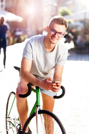 Young hipster light-hair boy in glasses sitting on the green bicycle at sunny summer streetの写真素材