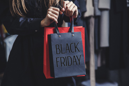 Woman wears black coat holding black friday bag before shop clothes background, sale conceptの写真素材