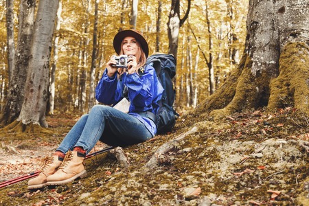 Young beautiful woman wearing hat and blue cloak with walking sticks in a forest, having a break, shootingの写真素材