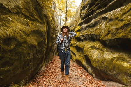 Travel young woman wearing brown hat, plaid shirt, jeans and brown boots with backpack ready to taking picture of wonderful canyon with moss on rocks after hiking, travelling conceptの写真素材