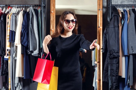 Fashion young brunette hair girl wearing sunglasses showing on the discount clothes in the shopping center, black friday conceptの写真素材